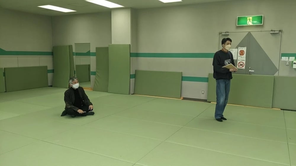 Iwanuma City General Gymnasium in Miyagi Prefecture. Professor Emeritus Kushi sits on a floor laid with green mats.