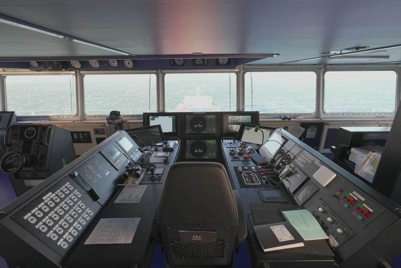 Photo: Daytime view of GENBU’s bridge, showing a central captain’s chair surrounded by advanced navigation consoles and screens, with the sea visible through large front windows.