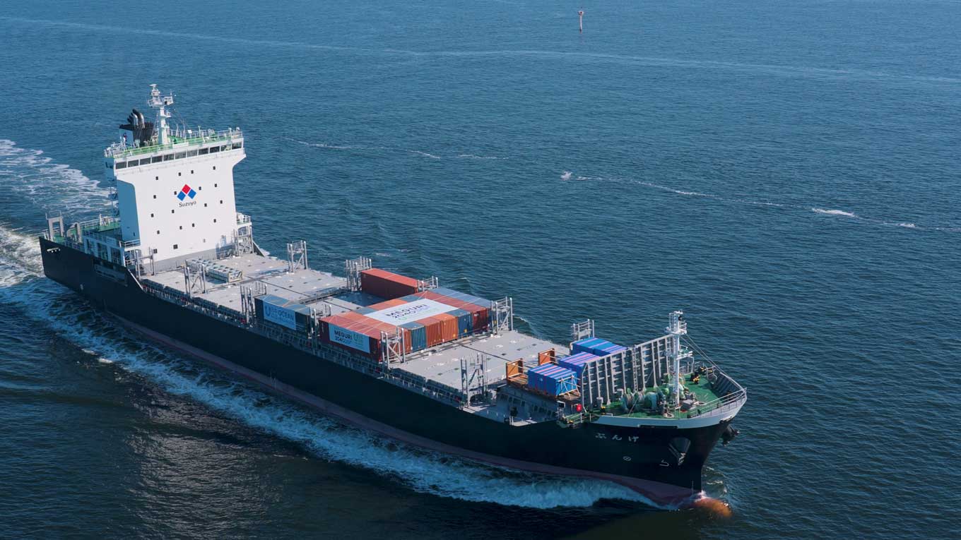 Photo: An aerial view of GENBU, a container ship carrying cargo containers, sailing at sea during daytime operations.