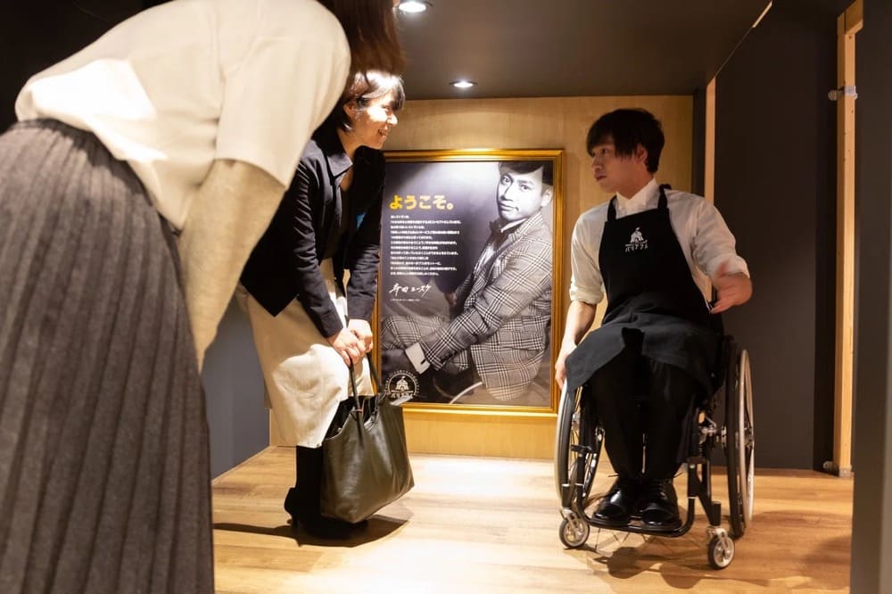 A restaurant staff member in a wheelchair guides visitors walking on two feet