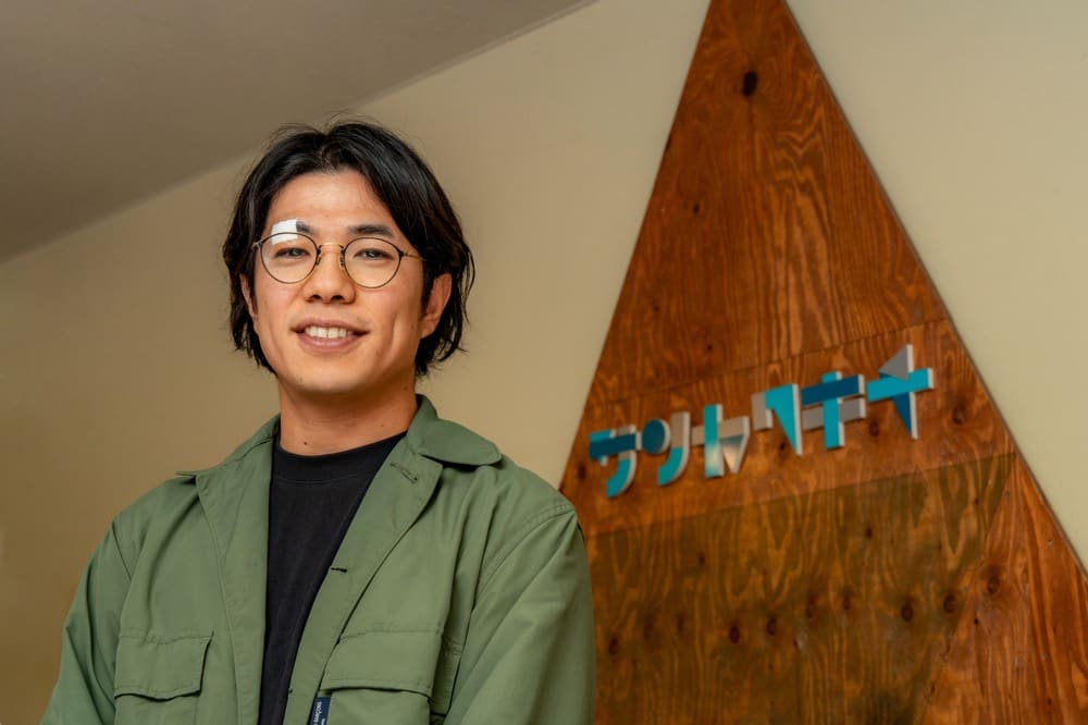 Yusuke Arai in front of the Sankakusha signboard