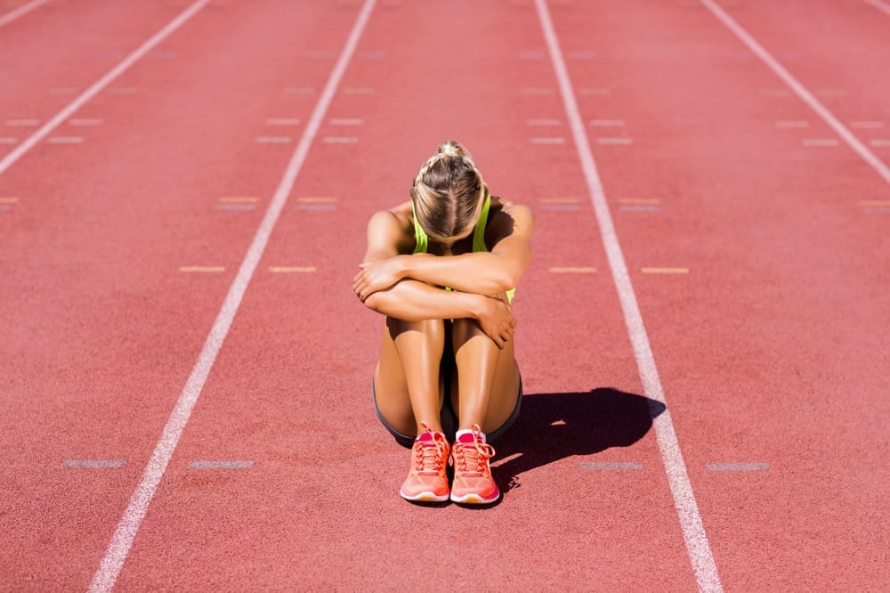 A female athlete sitting on a track holding her knees and crying