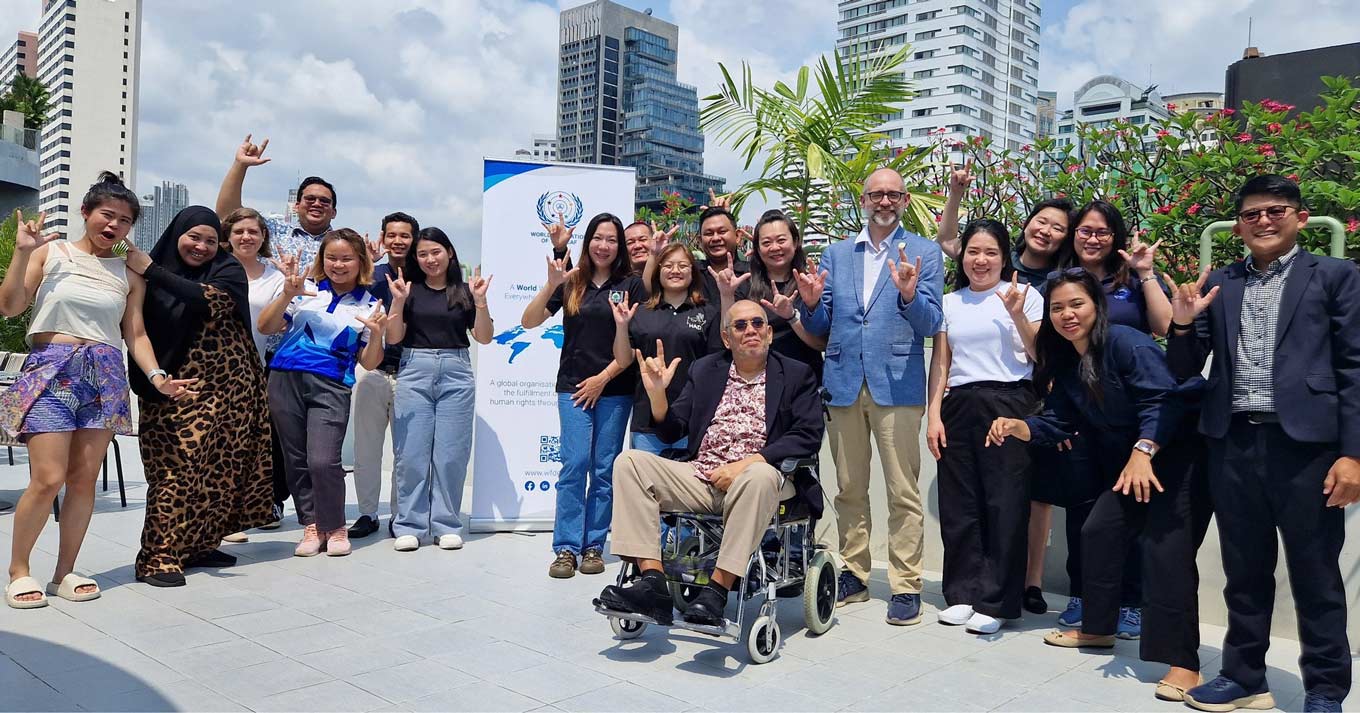 Photo: Participants in a regional workshop on legal recognition of sign languages pose together outdoors in front of a city skyline in February 2024.