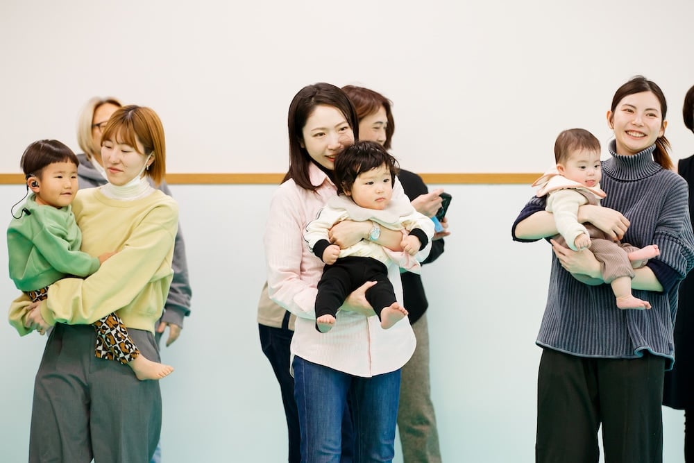 Mothers taking part in Baby Comekko while holding their children; the room is full of smiles