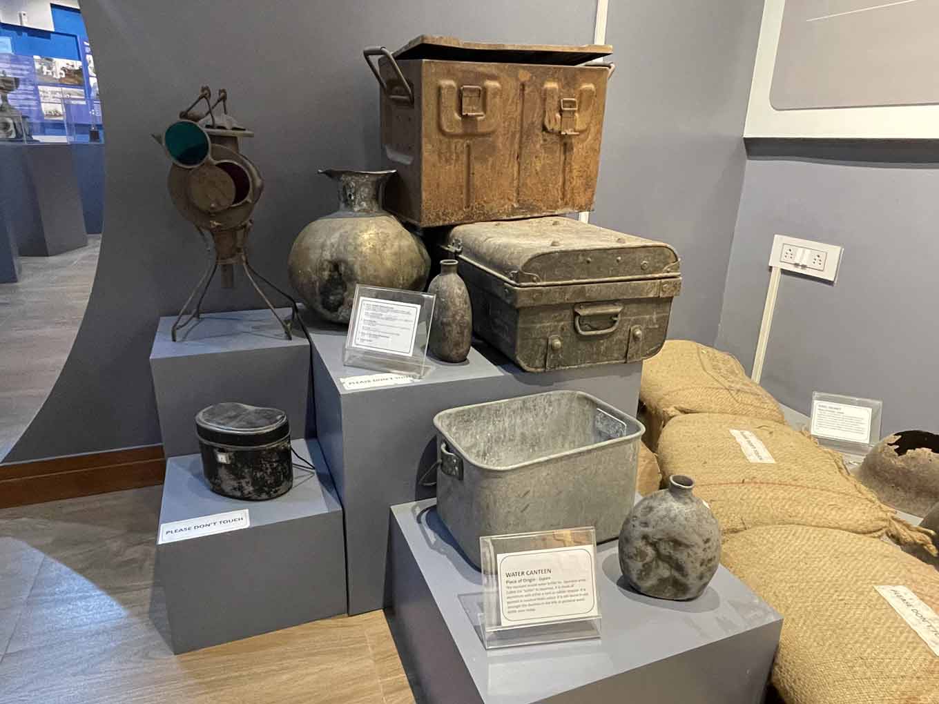 Photo of artifacts in the museum’s war section, including canteens, a military mess tin, metal storage boxes, and a signal lamp