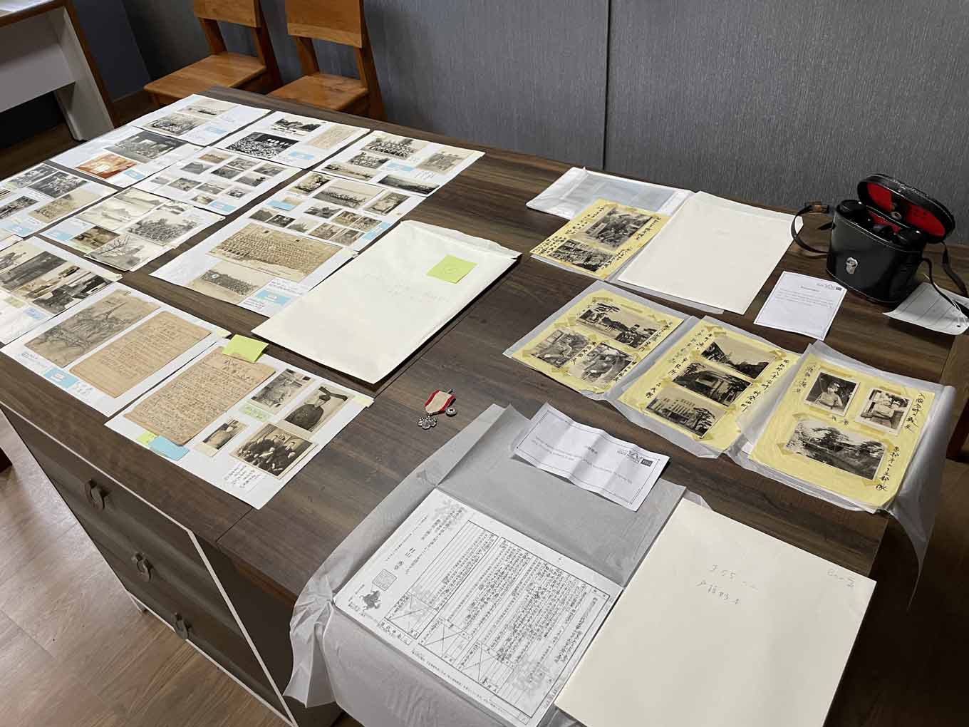 Photo of a table displaying items from the museum’s collection, including family register extracts, wartime photographs, badges, letters sent by soldiers to their families, and hand-drawn sketches